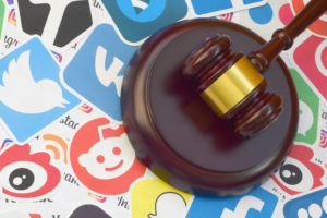 Wooden judge gavel lies on many paper logos of popular social networks and internet resources