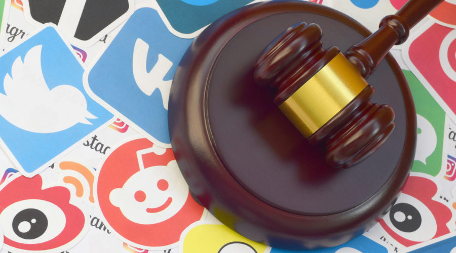 Wooden judge gavel lies on many paper logos of popular social networks and internet resources