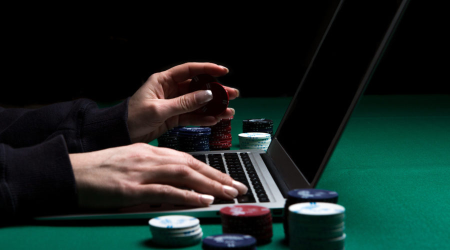 Woman playing online poker with laptop on a green table with chips all around, side view