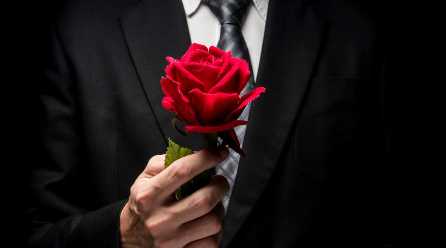 close up of man in black suit holding red rose