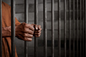 man clinching bars in jail cell