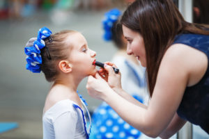 Mom paints lips with the lipstick of her little daughter before the dance performance.