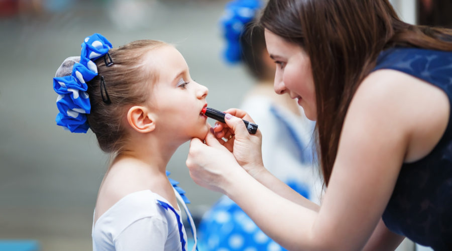 Mom paints lips with the lipstick of her little daughter before the dance performance.